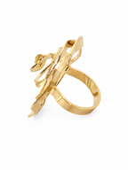 A gold-plated statement ring featuring a sculptural, abstract openwork design with a curved band and a central floral-like element, shown on a plain white background.